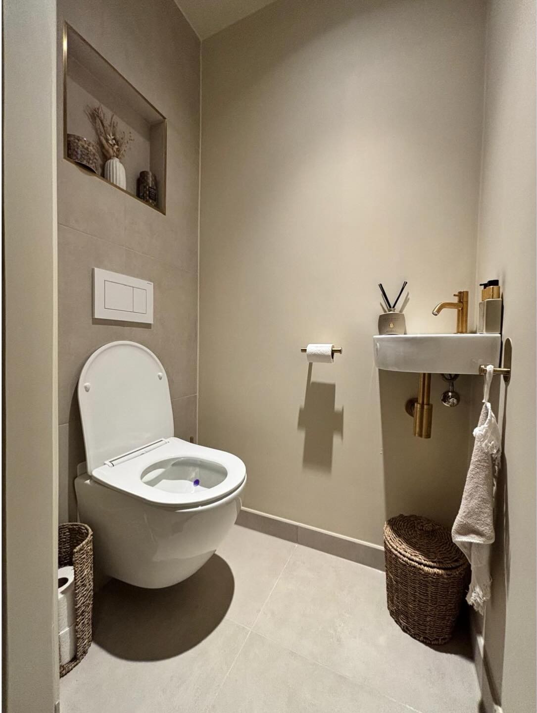 Toilet in warme grijstinten met nis, fonteintje en koperkleurige kraan in Delfstrahuizen