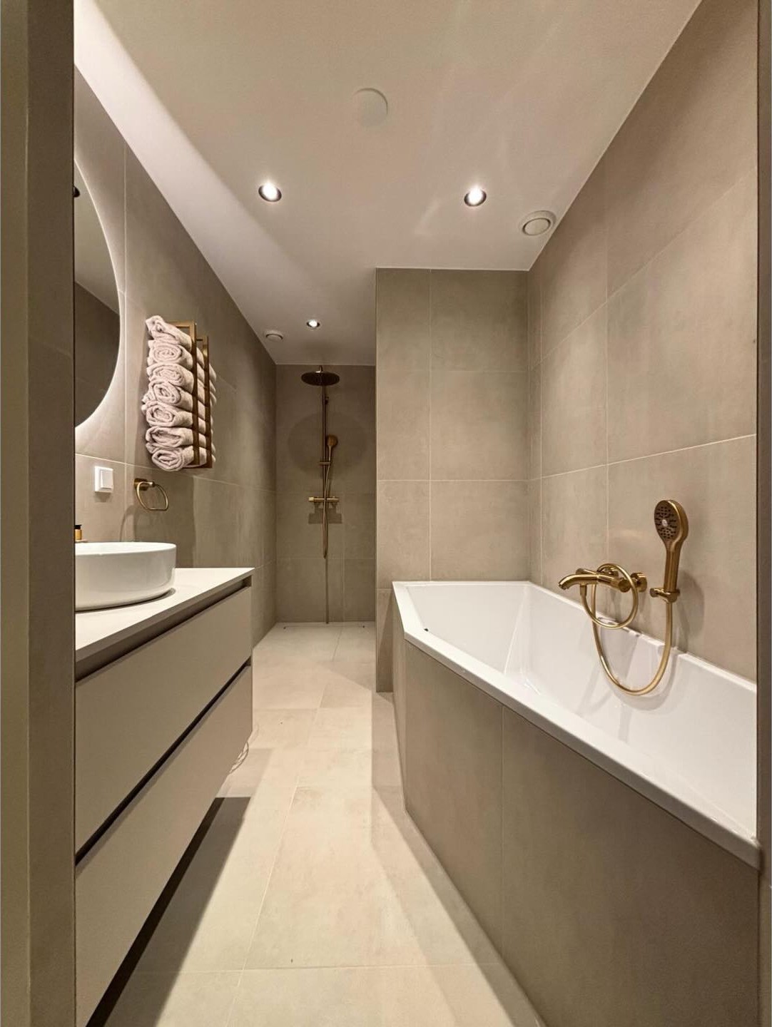 Lange badkamer in beige tinten met ligbad, wastafelmeubel en goudkleurige kranen in Delfstrahuizen